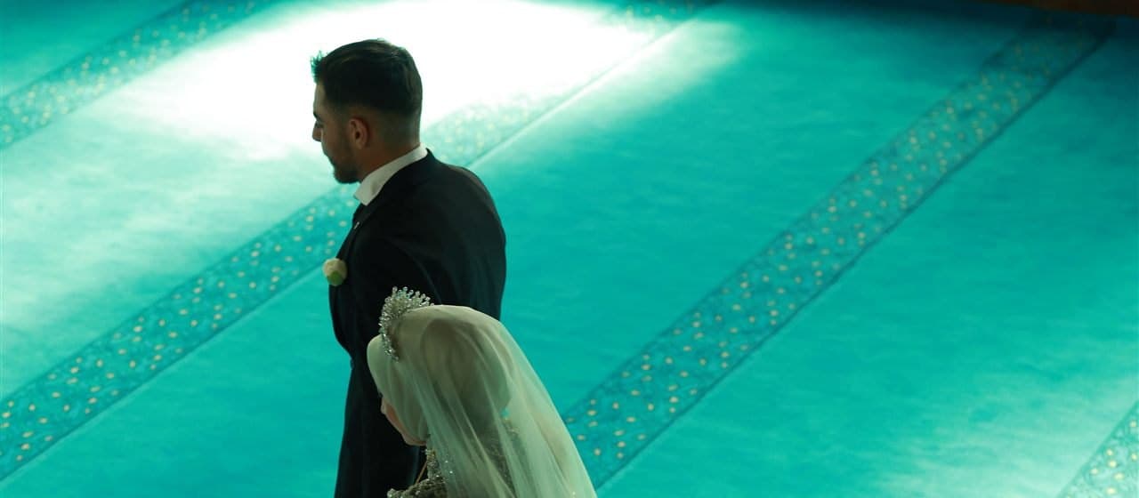 A bride and groom walking together across the prayer hall of a mosque